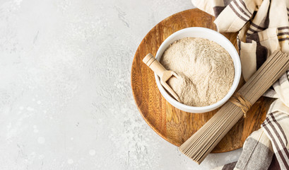 Buckwheat flour in bowl, small wooden scoop with flour and dried soba noodles. Healthy diet, gluten free products. Top view.