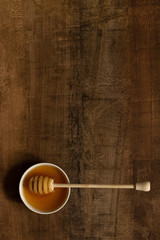 Honey in a bowl with a spoon on a warm color wooden table. Useful sugar substitute