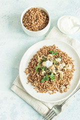 Buckwheat porridge with mushrooms and herbs in a ceramic plate on light grey concrete background. Vegan and vegetarian meal. Healthy content. Toned image. 