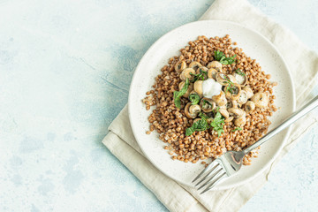 Buckwheat porridge with mushrooms and herbs in a ceramic plate on light grey concrete background. Vegan and vegetarian meal. Healthy content. Toned image. Top view. 
