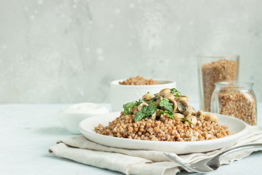 Buckwheat porridge with mushrooms and herbs in a ceramic plate on light grey concrete background. Vegan and vegetarian meal. Healthy content. Toned image. 