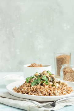 Buckwheat porridge with mushrooms and herbs in a ceramic plate on light grey concrete background. Vegan and vegetarian meal. Healthy content. Toned image. 