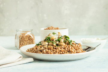 Buckwheat porridge with mushrooms and herbs in a ceramic plate on light grey concrete background. Vegan and vegetarian meal. Healthy content. Toned image. 