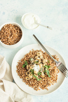 Buckwheat porridge with mushrooms and herbs in a ceramic plate on light grey concrete background. Vegan and vegetarian meal. Healthy content. Toned image. Top view. 