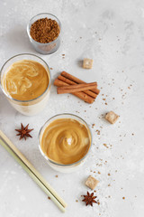 Iced Dalgona coffee in tall glass with spices. A trendy fluffy creamy whipped coffee. Korean coffee drink. Light grey concrete background.