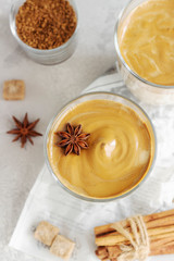 Iced Dalgona coffee in tall glass with spices. A trendy fluffy creamy whipped coffee. Korean coffee drink. Light grey concrete background. Top view.