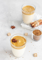 Iced Dalgona coffee in tall glass with spices. A trendy fluffy creamy whipped coffee. Korean coffee drink. Light grey concrete background.