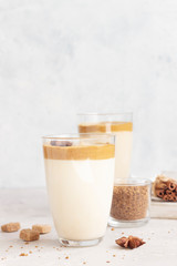 Iced Dalgona coffee in tall glass with spices. A trendy fluffy creamy whipped coffee. Korean coffee drink. Light grey concrete background. 