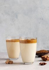 Iced Dalgona coffee in tall glass with spices. A trendy fluffy creamy whipped coffee. Korean coffee drink. Light grey concrete background.