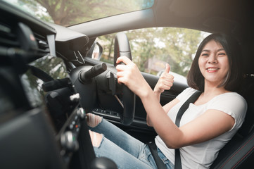 Happy smiling asian woman driving in her new car with confident showing thumb up