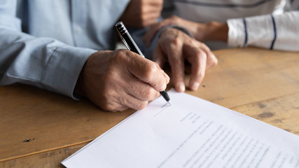 Close up older man putting signature on legal documents, mature couple, wife and husband making...