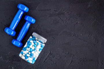 Dumbbells and creatine capsules - sport training concept - on black background top-down copy space