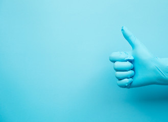 hand gesture of doctor wearing blue gloves on blue background, sign for good