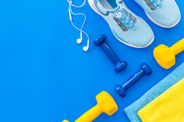 Fitness set with sneakers, dumbbells, towel on blue background top view copy space