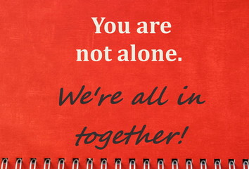 Inspirational quote you are not alone. we're all in together on red notebook background