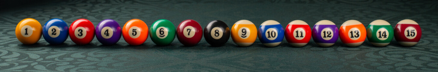 Billiard balls arranged in a row close-up on a green backgound. Wide frame.
