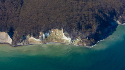 The famous chalk cliffs of the German Baltic Sea island of Rügen photographed from the air. At the bottom right is a small lighthouse and above the forest from the Jasmund National Park.
