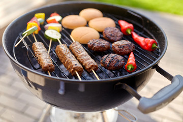 cooking, barbecue and food concept - close up of shish kebab meat, vegetables on bamboo skewers, burger buns and cutlets roasting on brazier grill outdoors