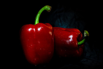 Two red bell peppers on black table with dark background. Front view