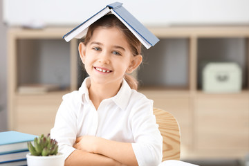 Cute little schoolgirl with book in classroom