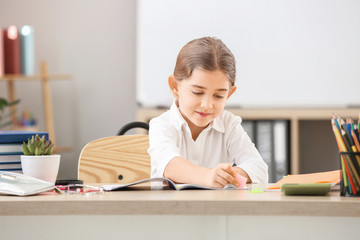 Fototapeta na wymiar Cute little schoolgirl doing task at desk in classroom