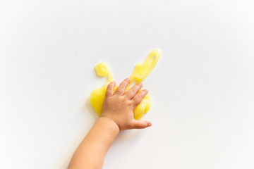 Top view of kid's hand and yellow slime on white background. Toddler activity. Motor skills. Homemade clay