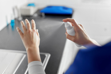 hygiene, healthcare and safety concept - close up of female doctor or nurse spraying antibacterial hand sanitizer at hospital
