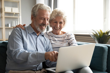 Excited older couple reading good news on social network or email, using laptop together, mature man and woman chatting or shopping online, browsing banking service, sitting on couch at home