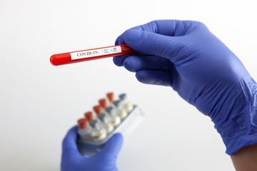 Coronavirus blood test concept. Doctor's hand in a medical glove holding a test tube with positive coronavirus blood over a laboratory desk. Coronavirus COVID-19. Pandemic.