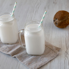 Coconut milk in glass jars on a white wooden background, low angle view.
