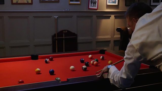 A Man Wearing A White Long Sleeves Polo Is Playing Billiards With A Backdrop Of Pictures On The Wall. -close up shot