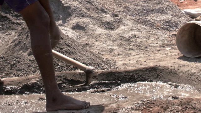 Closeup of man making concrete in a pit with a shovel - manual labour