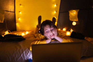 Little 11 year old girl using laptop under her home-made tent inside the living room.