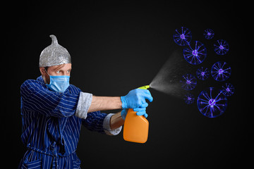 man in foil cap, gloves and medical mask fights coronavirus with spray detergent
