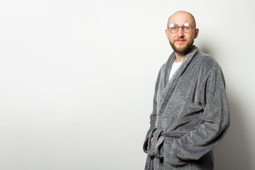 Portrait of a young bald man with a beard in a bathrobe and glasses on an isolated light background. Emotional face
