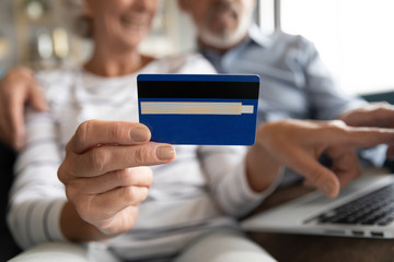 Close up mature couple paying online, older female holding plastic credit card in fingers, elderly man and woman using laptop, shopping, booking hotel, using internet banking service, making payment