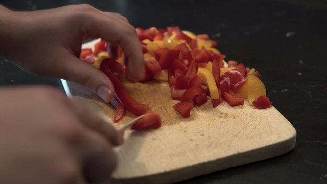 A man slices coloured peppers on a wooden board, close up