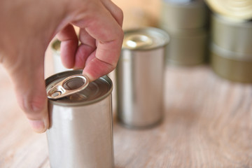 Hand open canned food in metal can on wooden background Close up canned goods non perishable food...