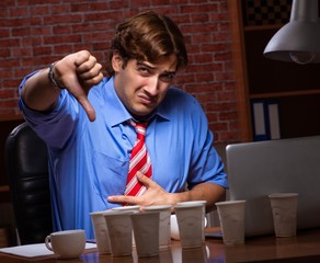 Young employee drinking coffee working at night shift