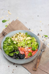 Poke bowl with smoked salmon, cucumber, avocado, sea kale, bean sprouts, sesame and herbs. Grey background, copy space.