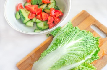 Chinese cabbage and vegetable salad on wooden cutting board. Vegetables on white table. Healthy vegetarian food. Fresh vegetables. Diet concept. Easy veheterian salad. Cooking a simple salad.