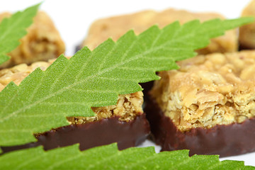 Sweet cannabis candy CBD Cannabidiol next to green leaves of marijuana on white isolated background. Candy with the addition of medical cannabis CBD for recreational use to relax body and mind