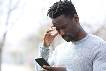 Worried black man reading bad news on phone at park