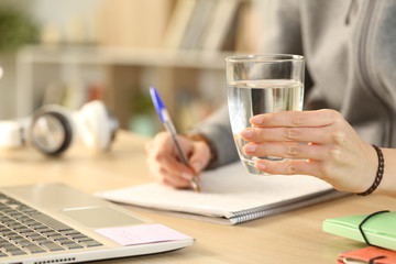 Fototapeta premium Student hands holding glass of water studying with notebook