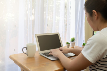 A young asian woman using computer to work from home in the living room in the morning during covid-19 or coronavirus pandemic