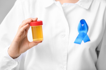 Doctor with cancer awareness ribbon holding urine sample in jar, closeup