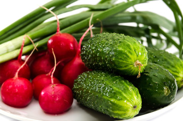 radish, cucumbers and green onions on a white plate. Close-up.