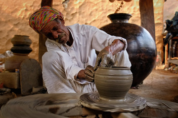 Indian potter at work: throwing the potter's wheel and shaping ceramic vessel and clay ware: pot,...