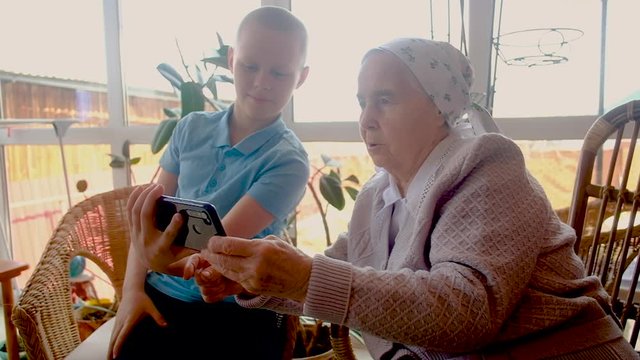 10-year-old grandson teaches an 80-year-old grandmother how to use a smartphone. playing with a smartphone. Make purchases online. are photographed. on the veranda of the house.