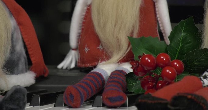 A group of cheerful dwarves sits on the piano against the background of a monitor with a New Year's toy. Homemade figurines made of fabric are placed on the piano keys. Camera movement from objects.